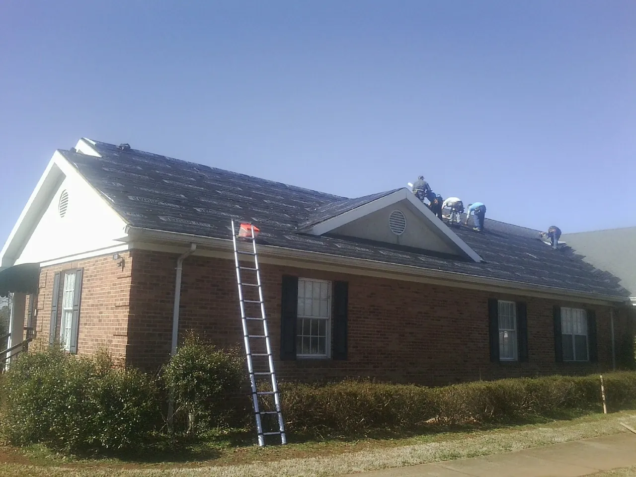 Crew tearing shingles off a brick ranch roof with a ladder set — Emergency Roof Repair work by our crew in Danube