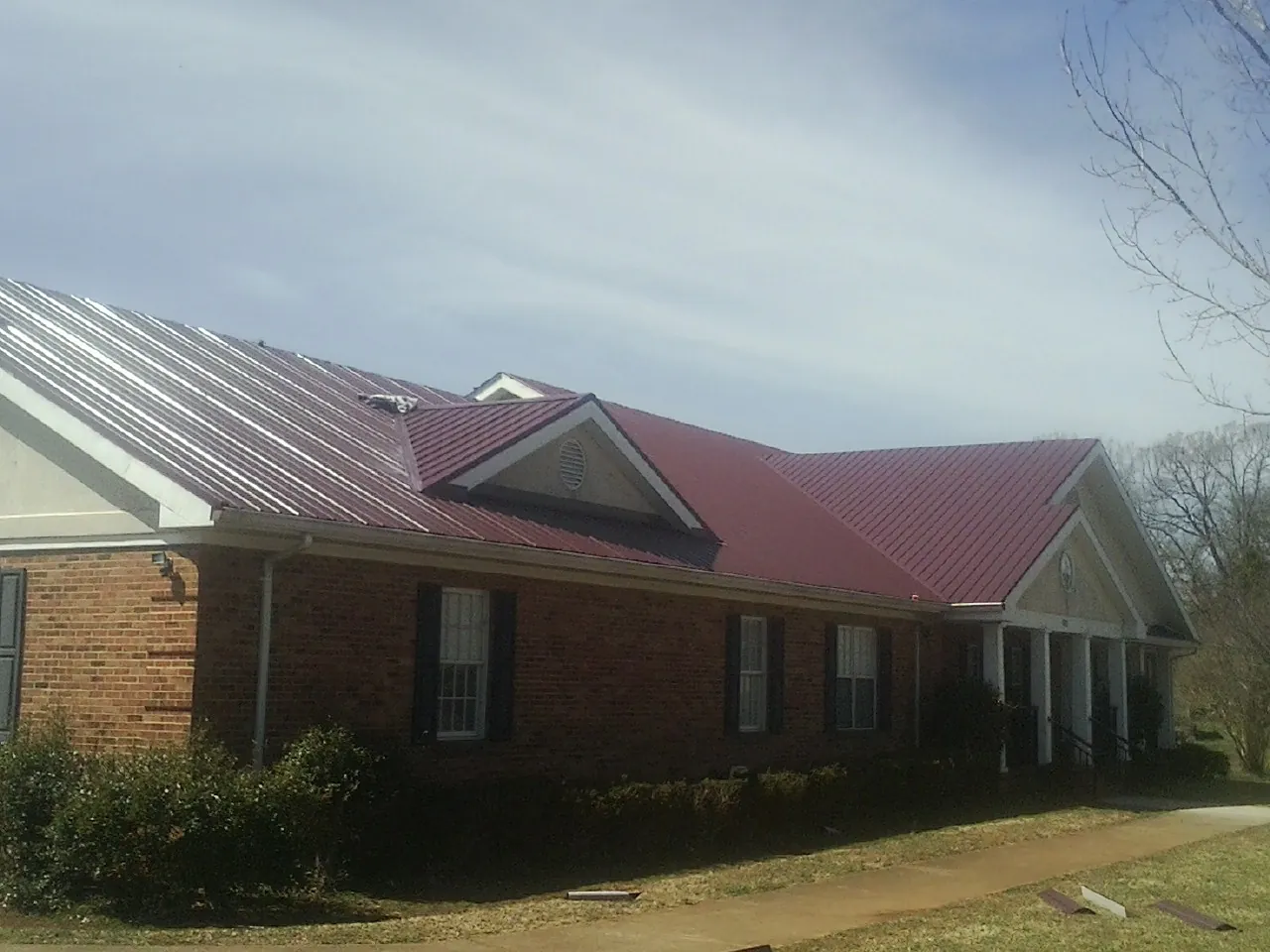 Red metal roof with gabled entries on a long brick building, from a Hail Damage Roof Repair job in Danube