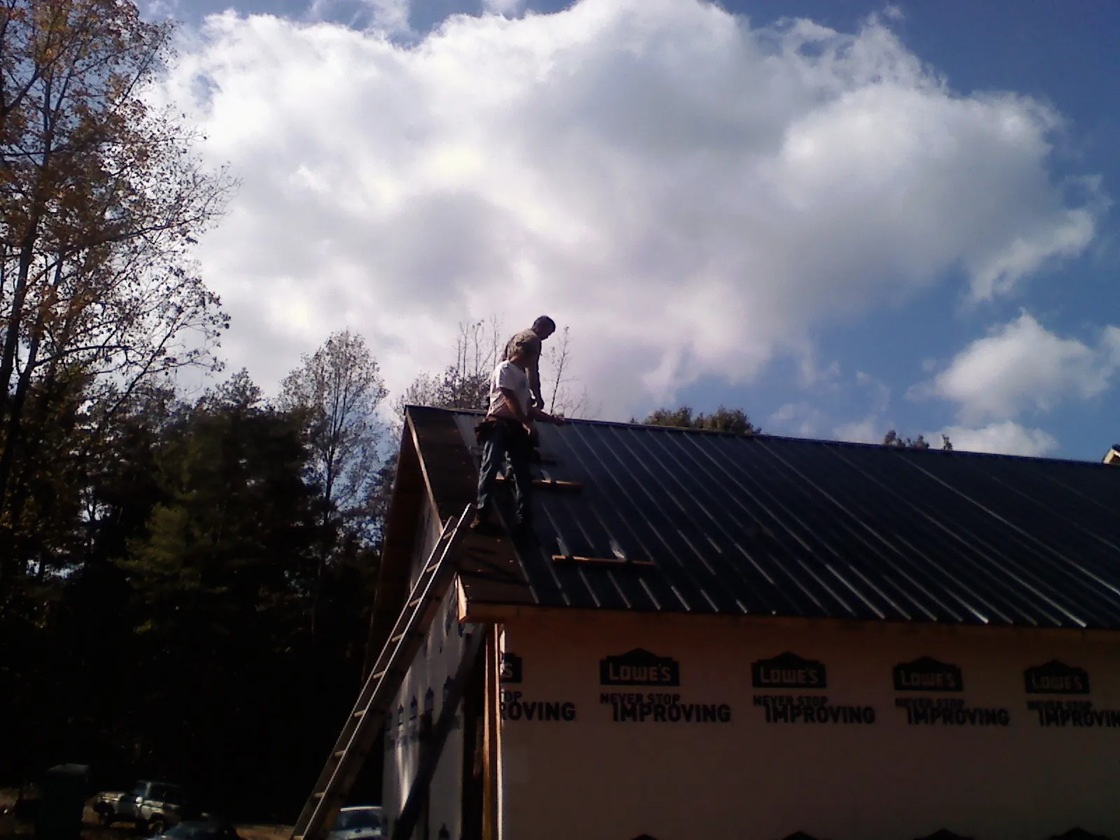 Roofer fastening dark metal panels high against a cloudy sky, from a Roof Inspection job in Danube