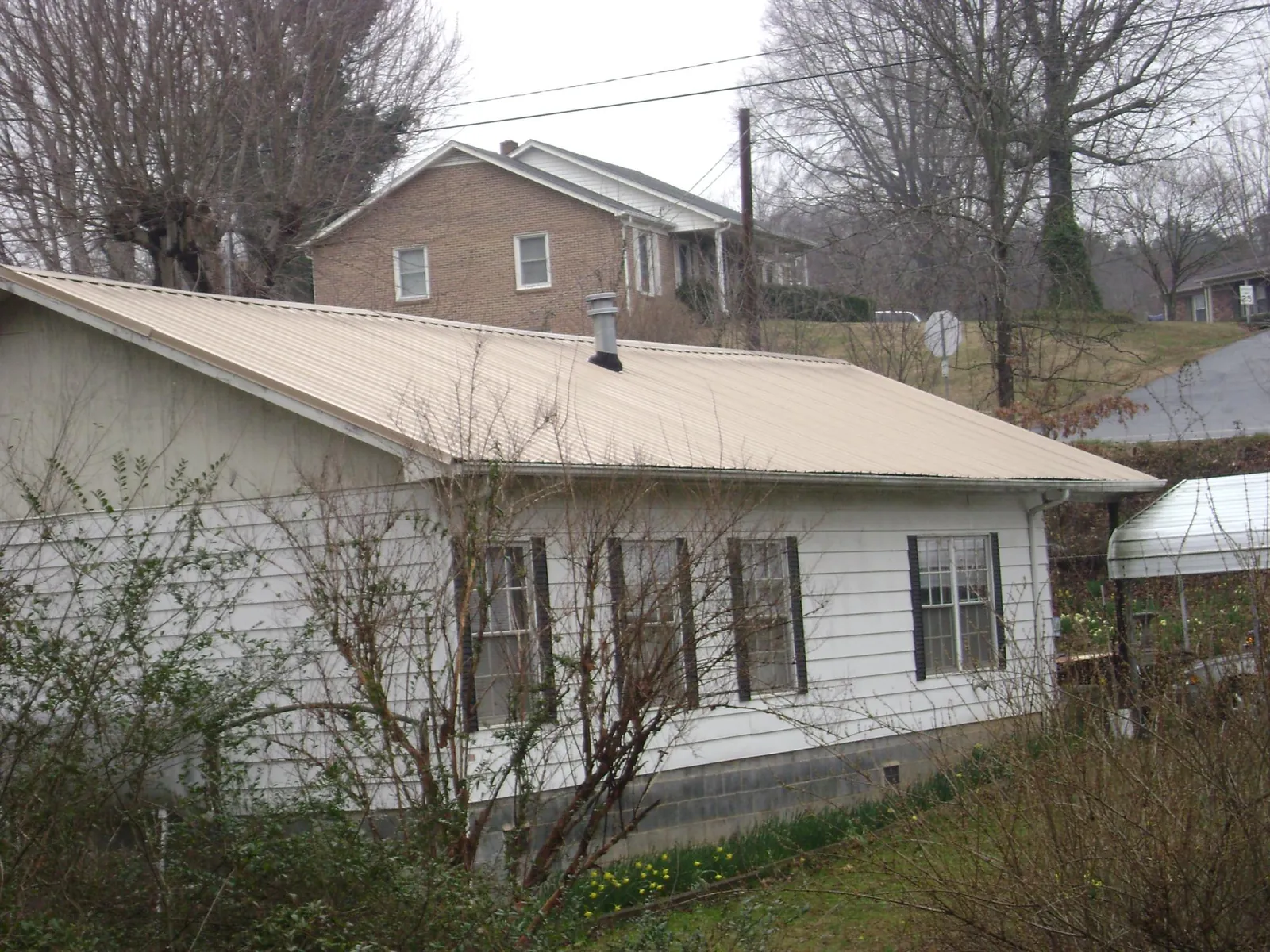 Tan metal roof on a white sided house set into a hillside — Commercial Roofing by Roofing Brothers in Danube